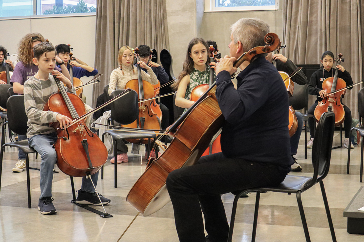 Man with a cello in front of students teaching