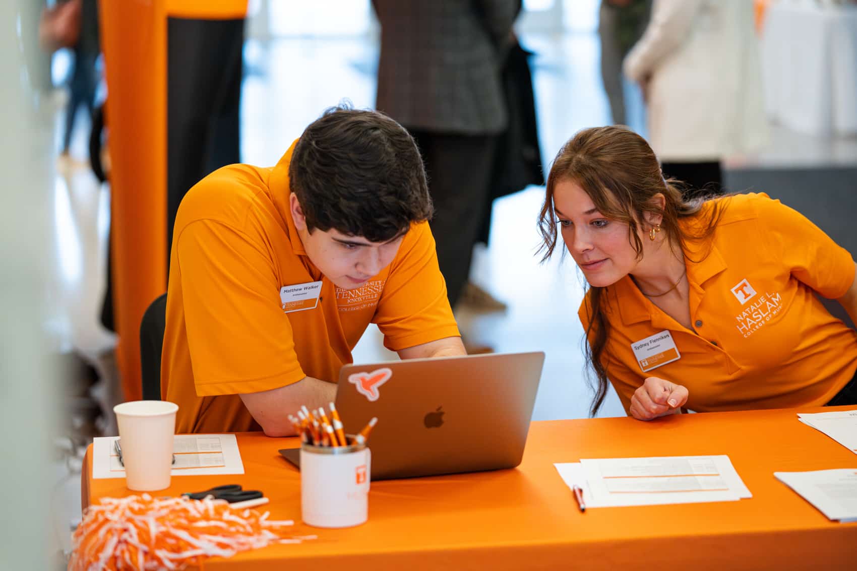 Male and female student in orange at check-in table looking over a computer