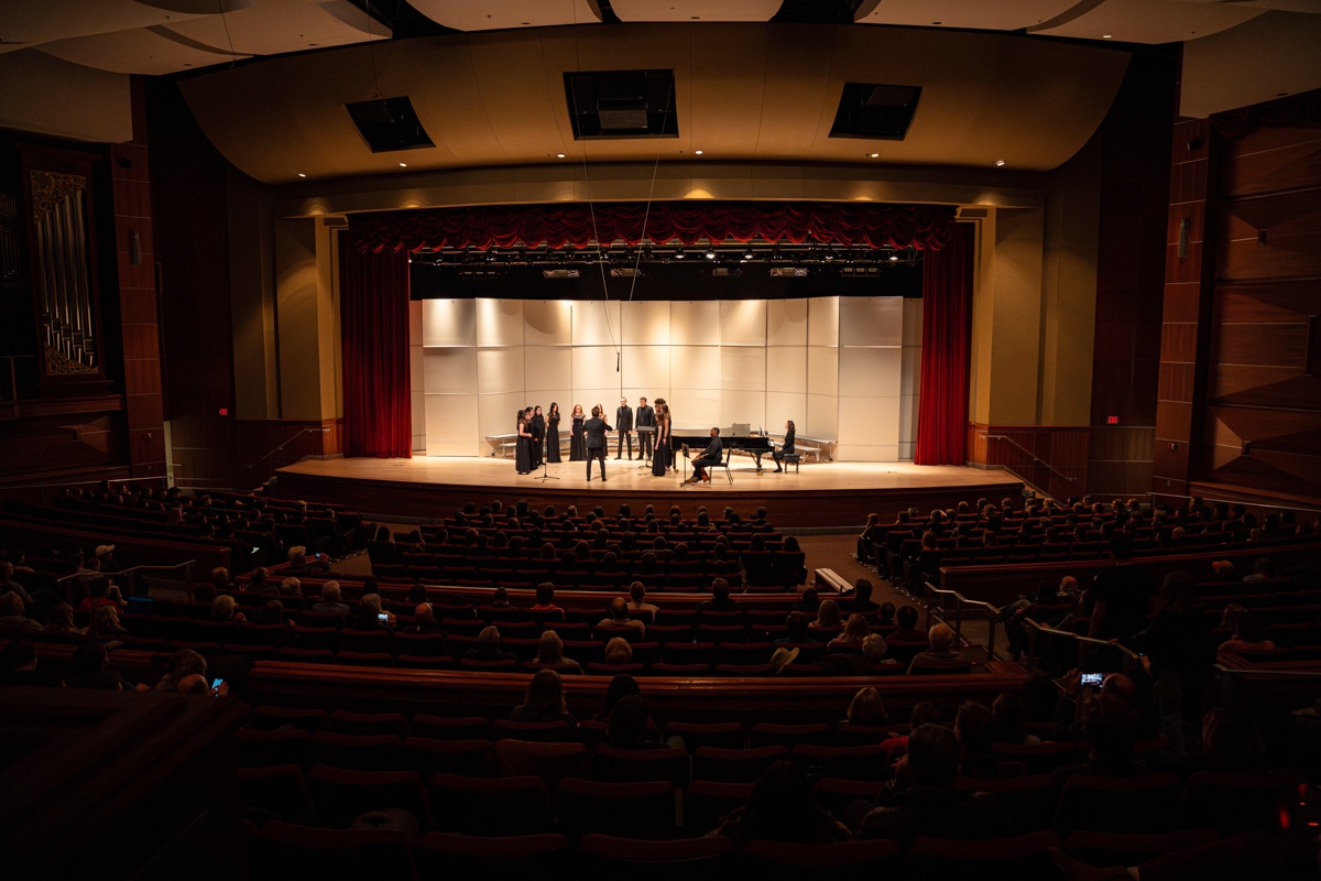 Auditorium and stage, with singers on the stage and folks in the audience watching