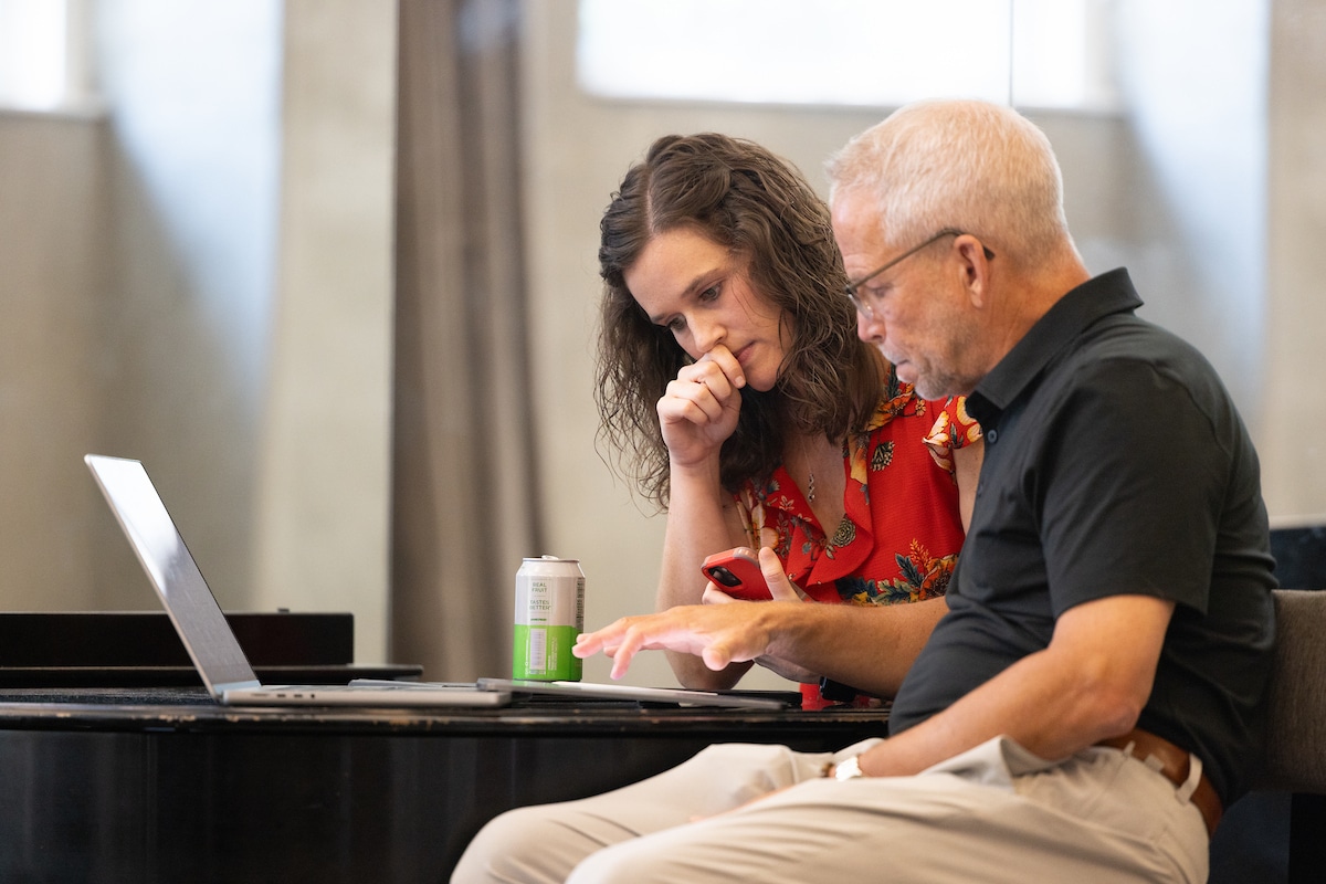 Man and woman look down at paper with a computer in front of them.