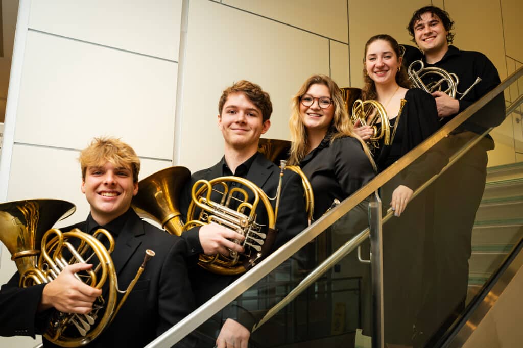 Group of students posing on a stair case with their french horns.