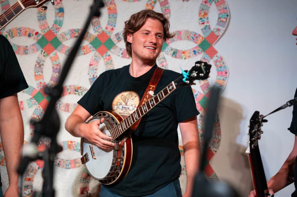Male musician holding banjo on a stage smiling