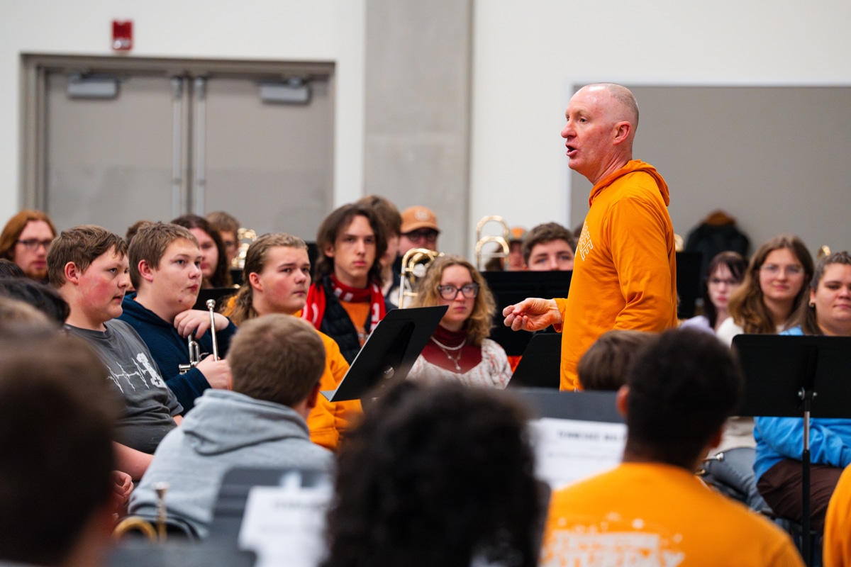 Male professor in orange in front of a group of band students teaching