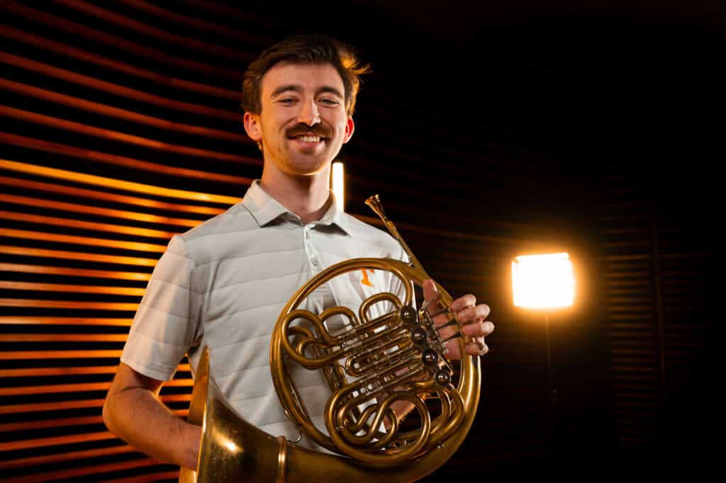 Photo of student with french horn smiling.