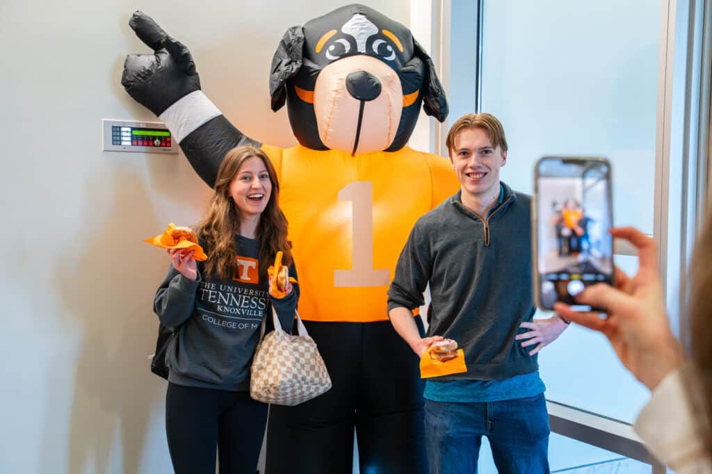 Female and male student posing in front of inflatable Smokey while a person takes a photo with a phone