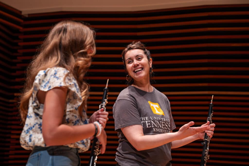 Female professor on stage smiling while teaching female student on stage with oboes