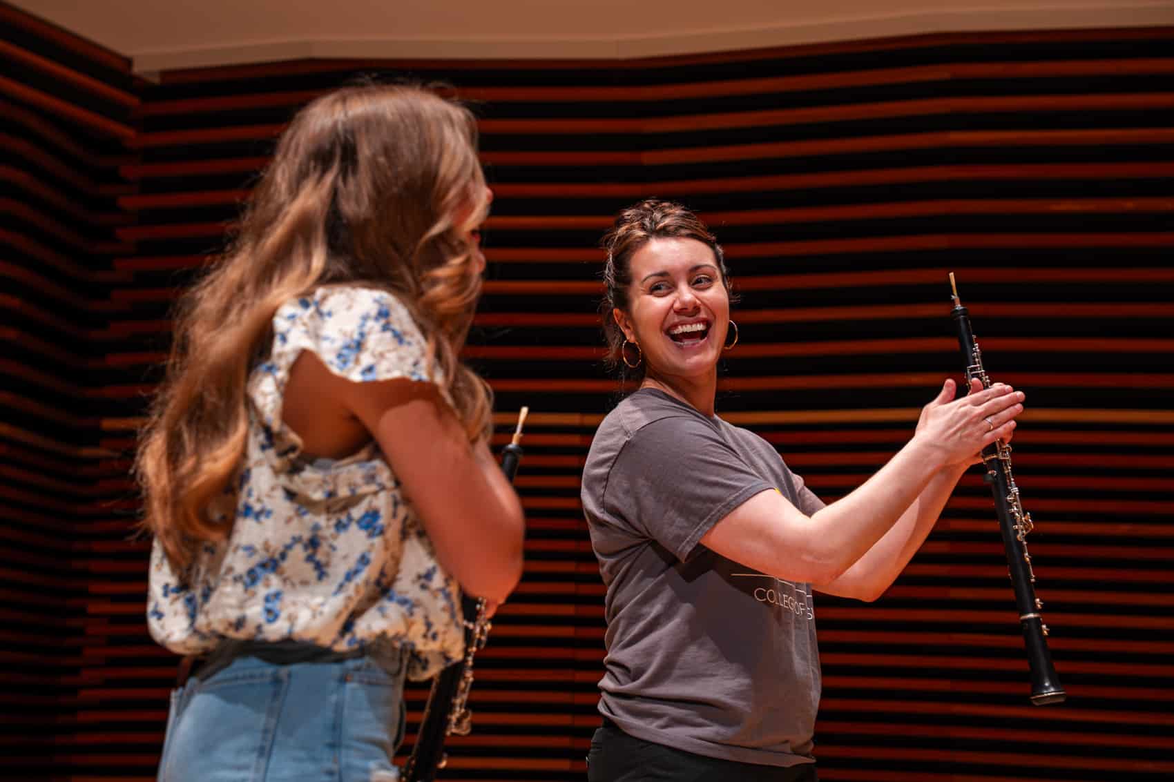 Professor Atherholt on stage smiling as she works with female student on the oboe.