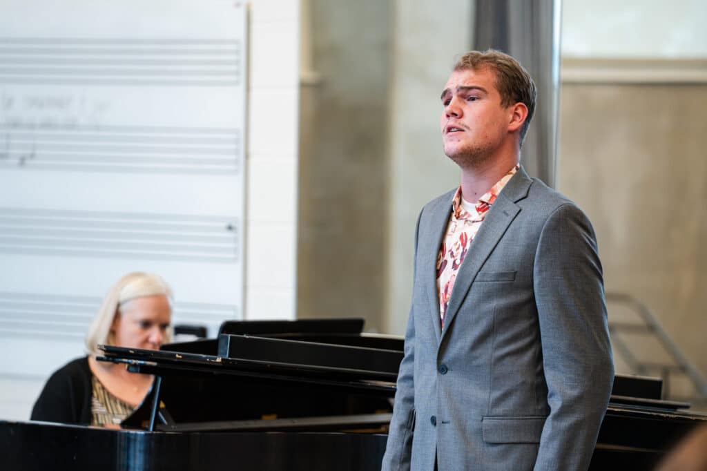 Male student singing with a pianist in the background