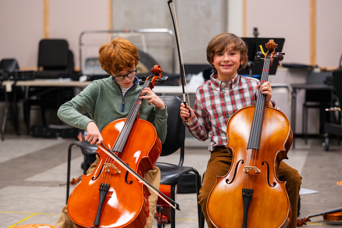 Two boys play the cello and smile