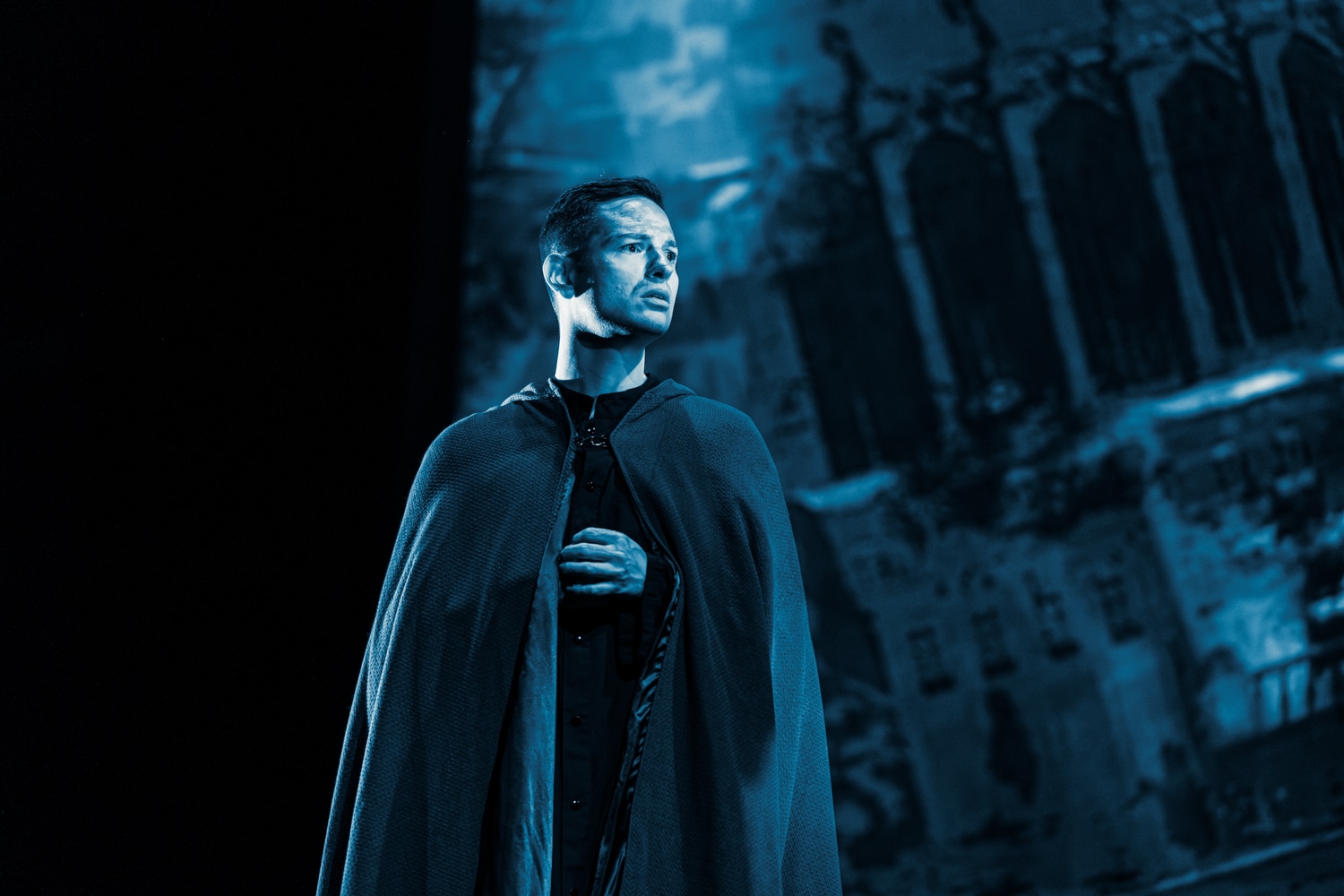 Man on stage performing in opera, in blue lighting.