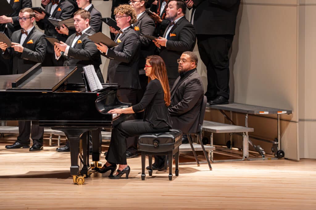 Pianist on stage playing alongside choral group.