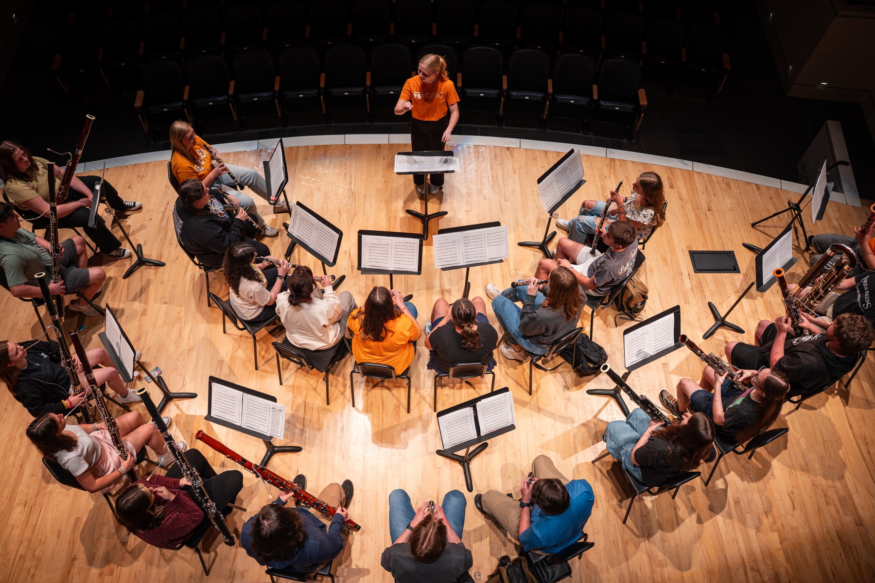UT student conducts group of young oboe players on stage, aerial view.