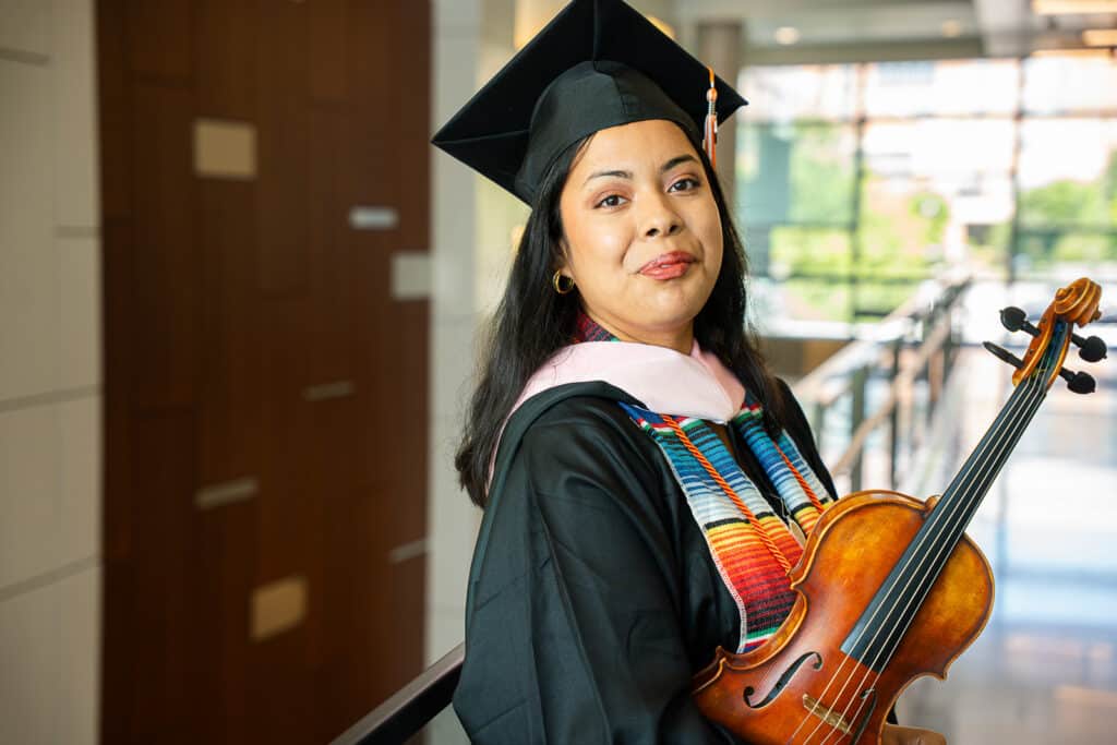 Student in regalia holding a violin.
